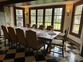 Un comedor con piso a cuadros, una mesa larga dispuesta para seis personas y ventanas grandes con vistas al verdor.