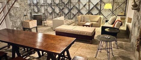 A cozy living room with a stone wall, a wooden dining table, and a sofa.
