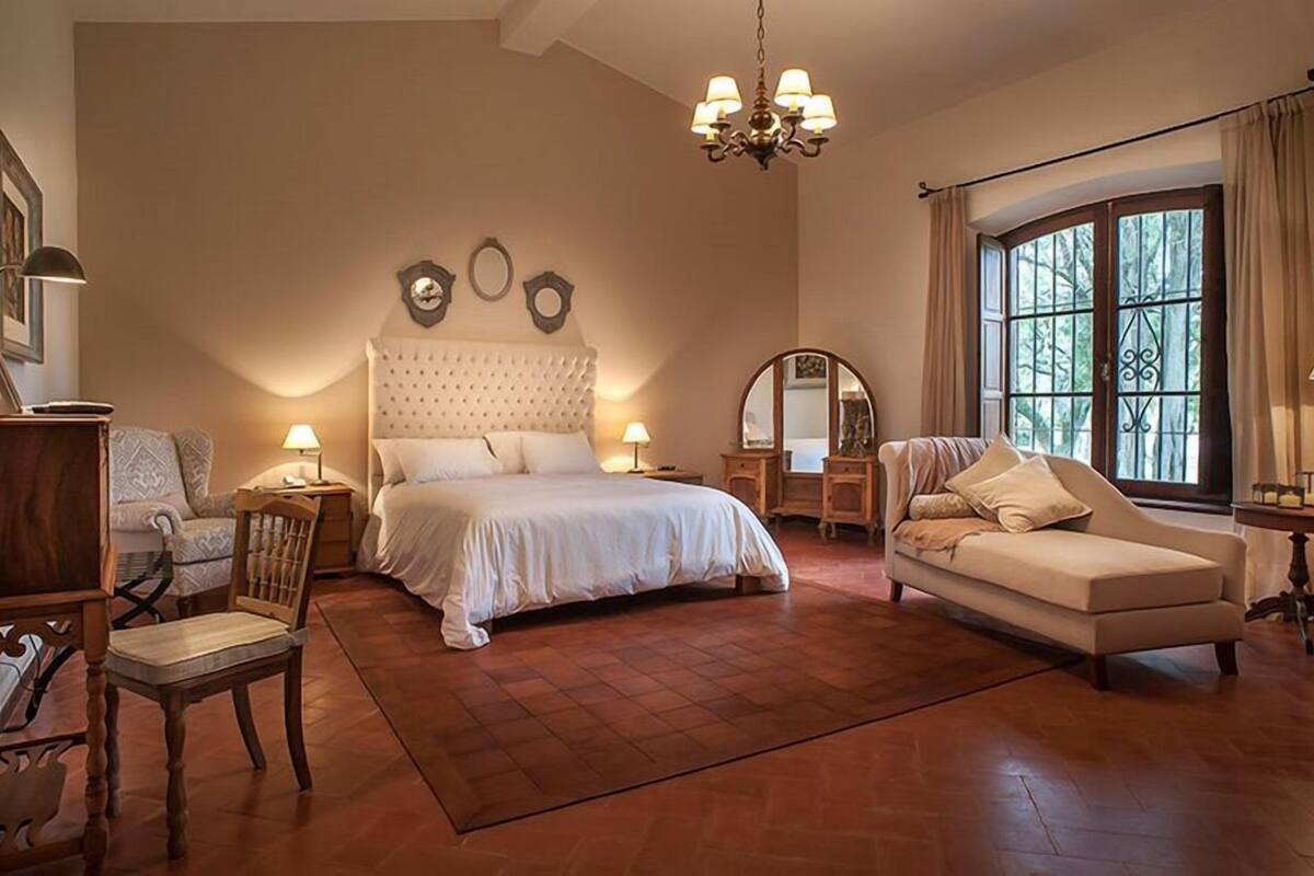 A spacious bedroom with a large bed, a sitting area with a sofa, and a dining area with a table and chairs.