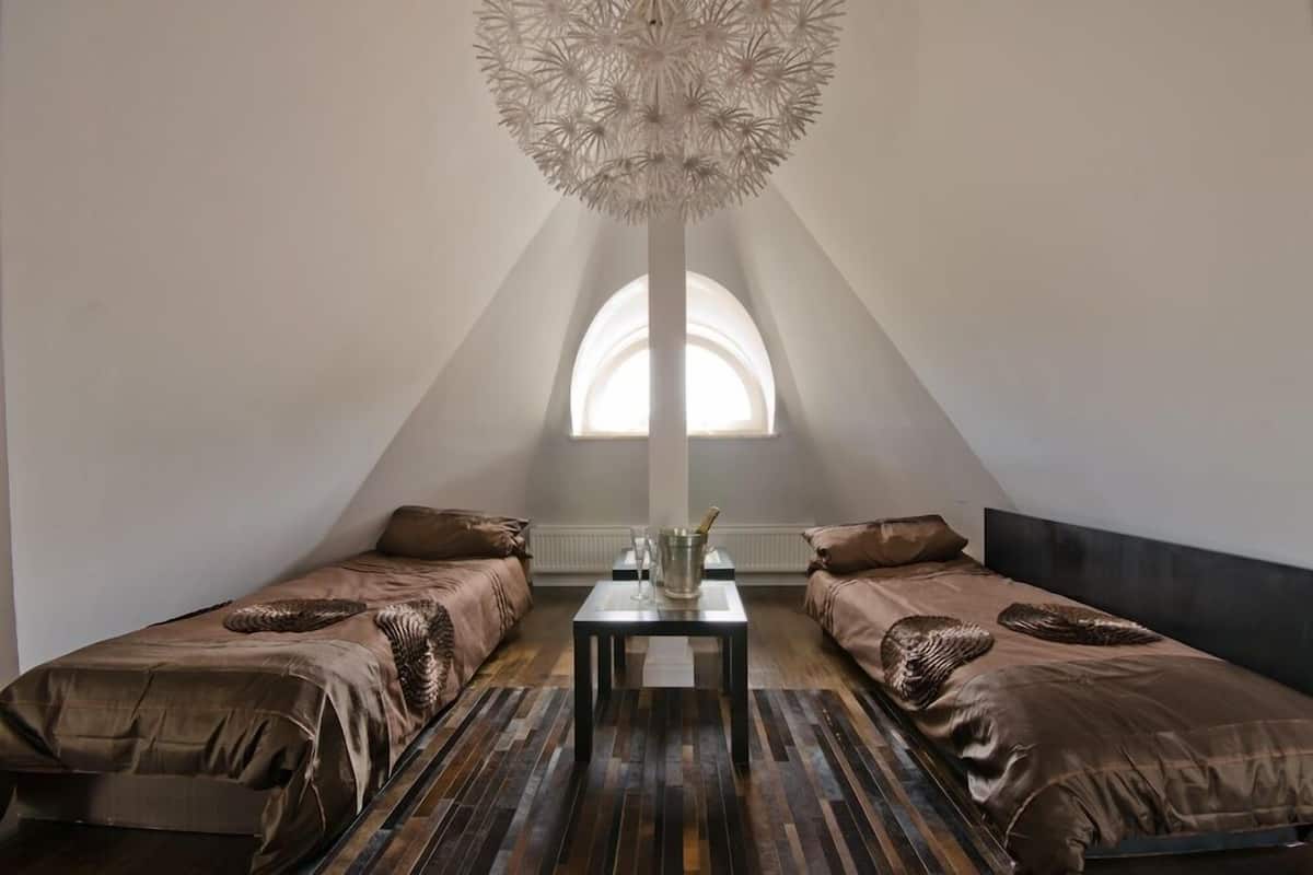 A modern, minimalist room with two beds, a central table, and a unique ceiling light fixture.