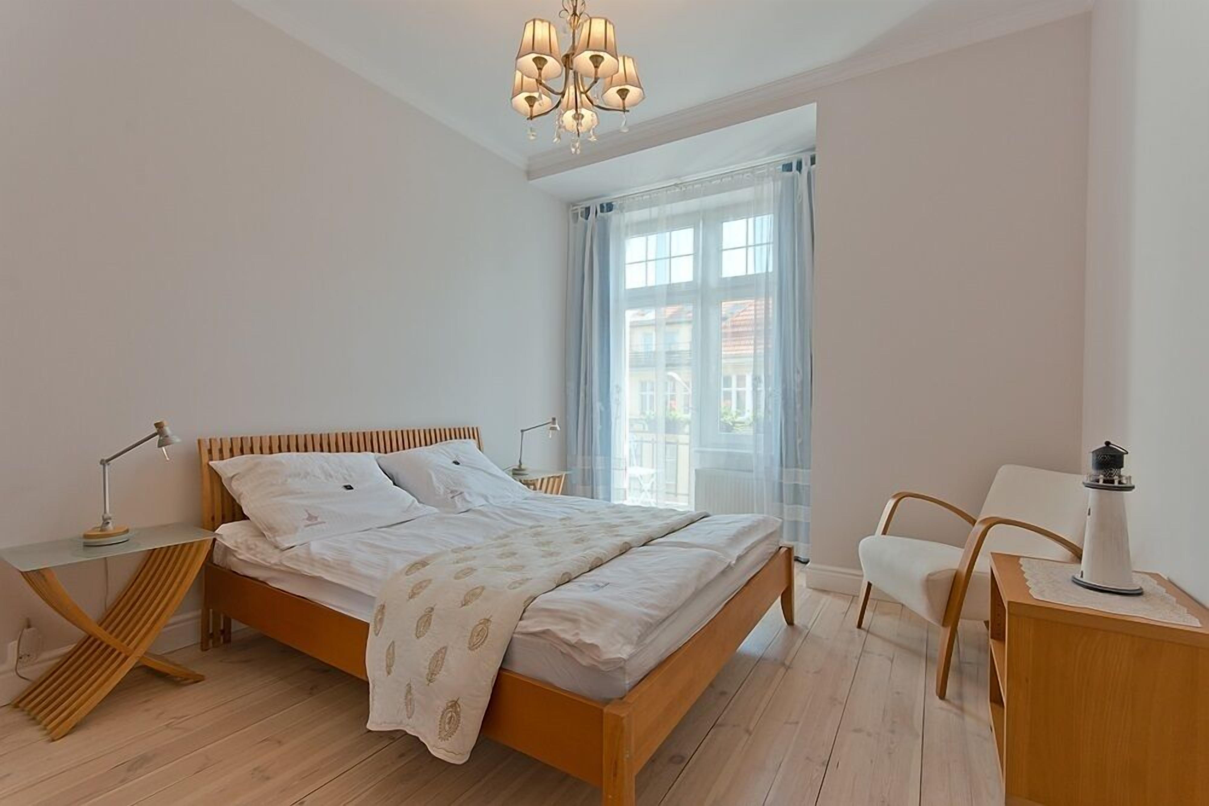 A bedroom with a wooden bed, a desk with a lamp, a chair, and a window with curtains.
