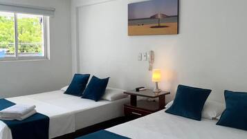 A hotel room with two beds, a window, a painting, a bedside table with a lamp, and a ceiling fan.