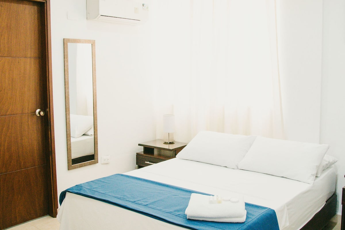 A hotel room with a bed, a nightstand, a mirror, a wardrobe, and a ceiling fan.