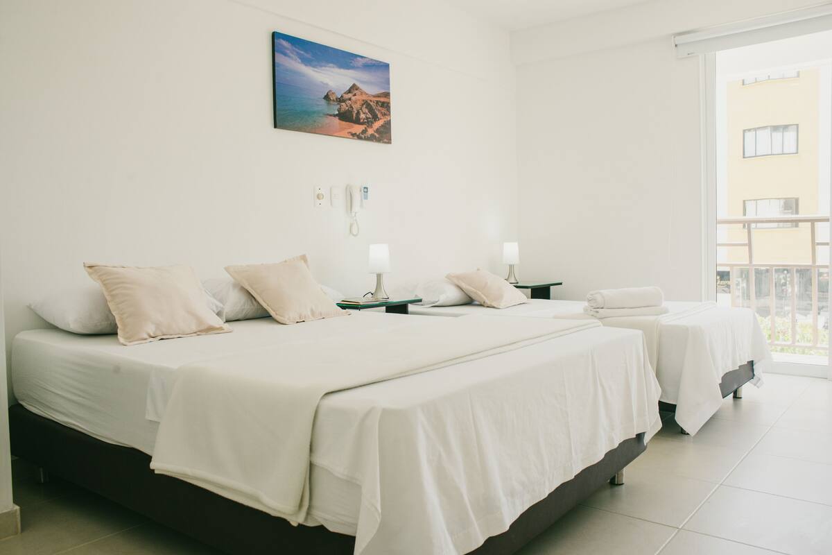 A hotel room with two beds, a phone, and a painting of a coastal landscape.