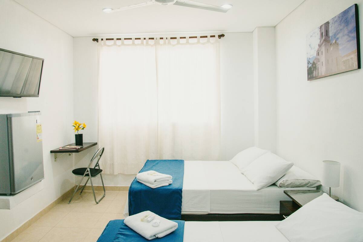 A hotel room with two beds, a desk, a chair, a TV, and a painting on the wall.