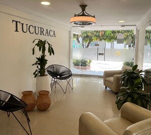 En modern interiör med en reception, inklusive en receptionsdisk, sittplatser och en vägg med namnet ”TUCURACA”.