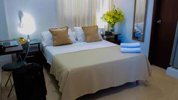 Une chambre d’hôtel avec un lit, un bureau avec un ordinateur portable, une valise, une lampe et un miroir.