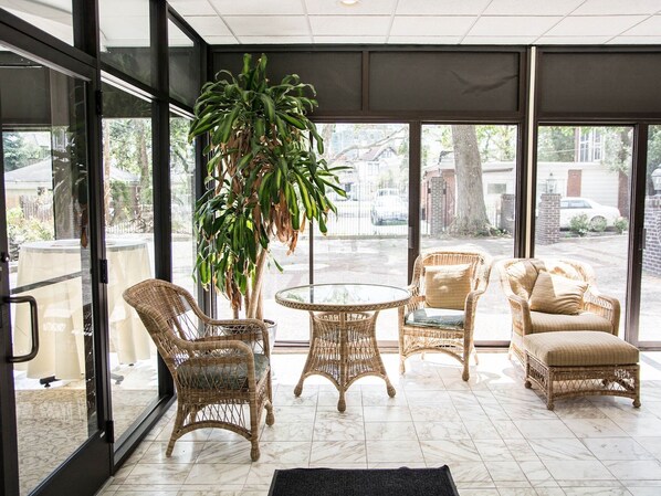 A room with wicker furniture, a glass table, and a large potted plant. - The Manor on Front (Harrisburg)
