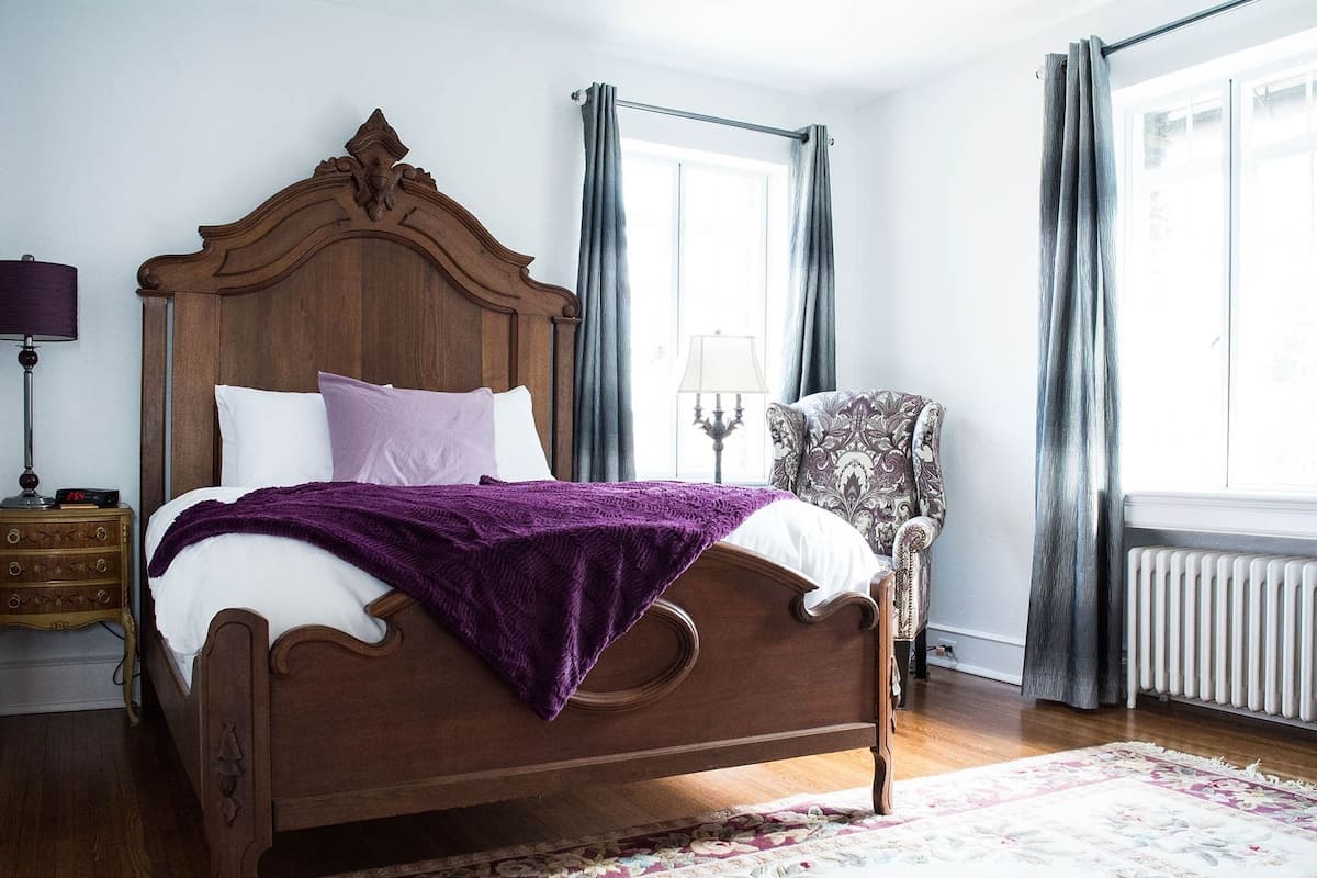 A bedroom with a wooden bed, a nightstand, a chair, and a window with curtains.