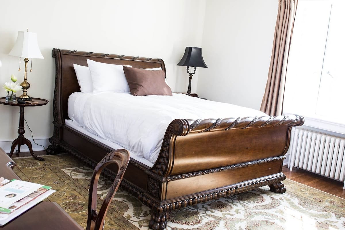 A neatly made bed with a wooden headboard, a bedside table with a lamp, and a window with curtains.