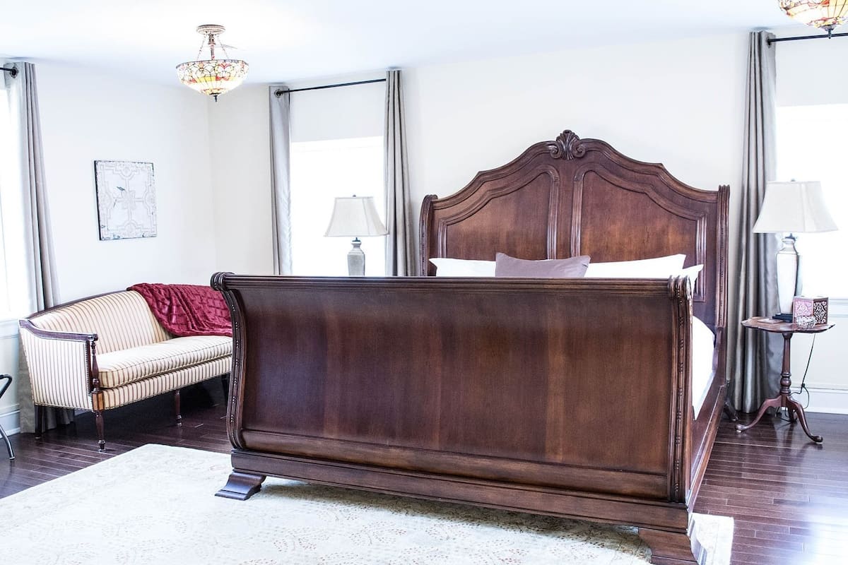 A bedroom with a large wooden bed, a striped sofa, a red throw blanket, and a chandelier.
