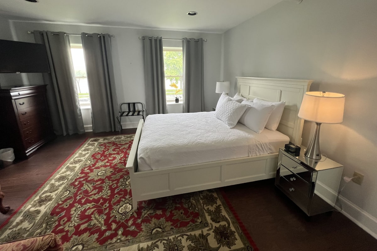 A neatly arranged hotel room with a large bed, a bedside table with a lamp, a dresser, and a chair.