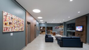 Un hall d’entrée moderne agrémenté d’un grand tableau abstrait, d’un téléviseur à écran plat et d’un espace salon avec des canapés et une table basse.