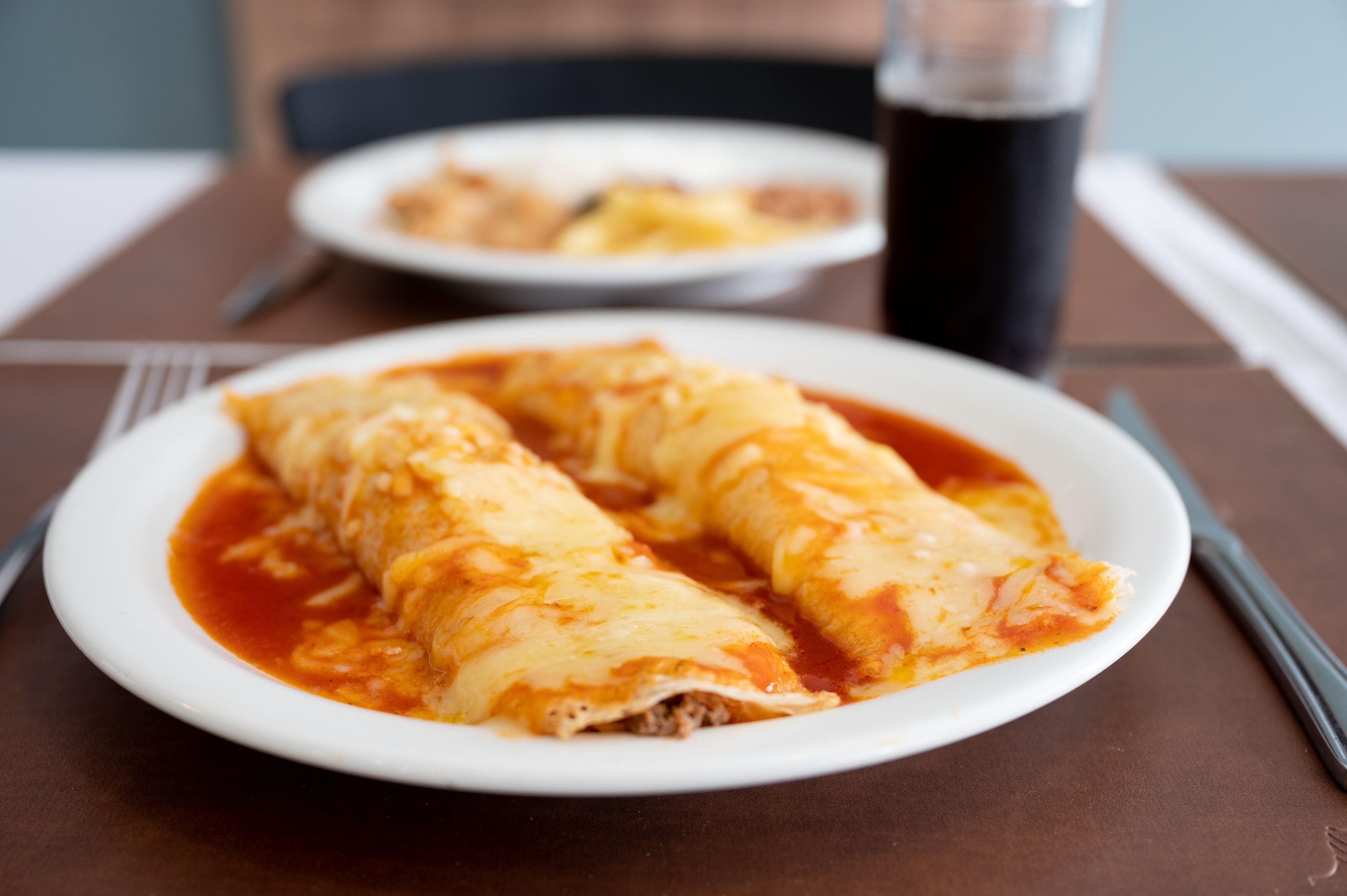 A plate of enchiladas with a glass of soda on a table.