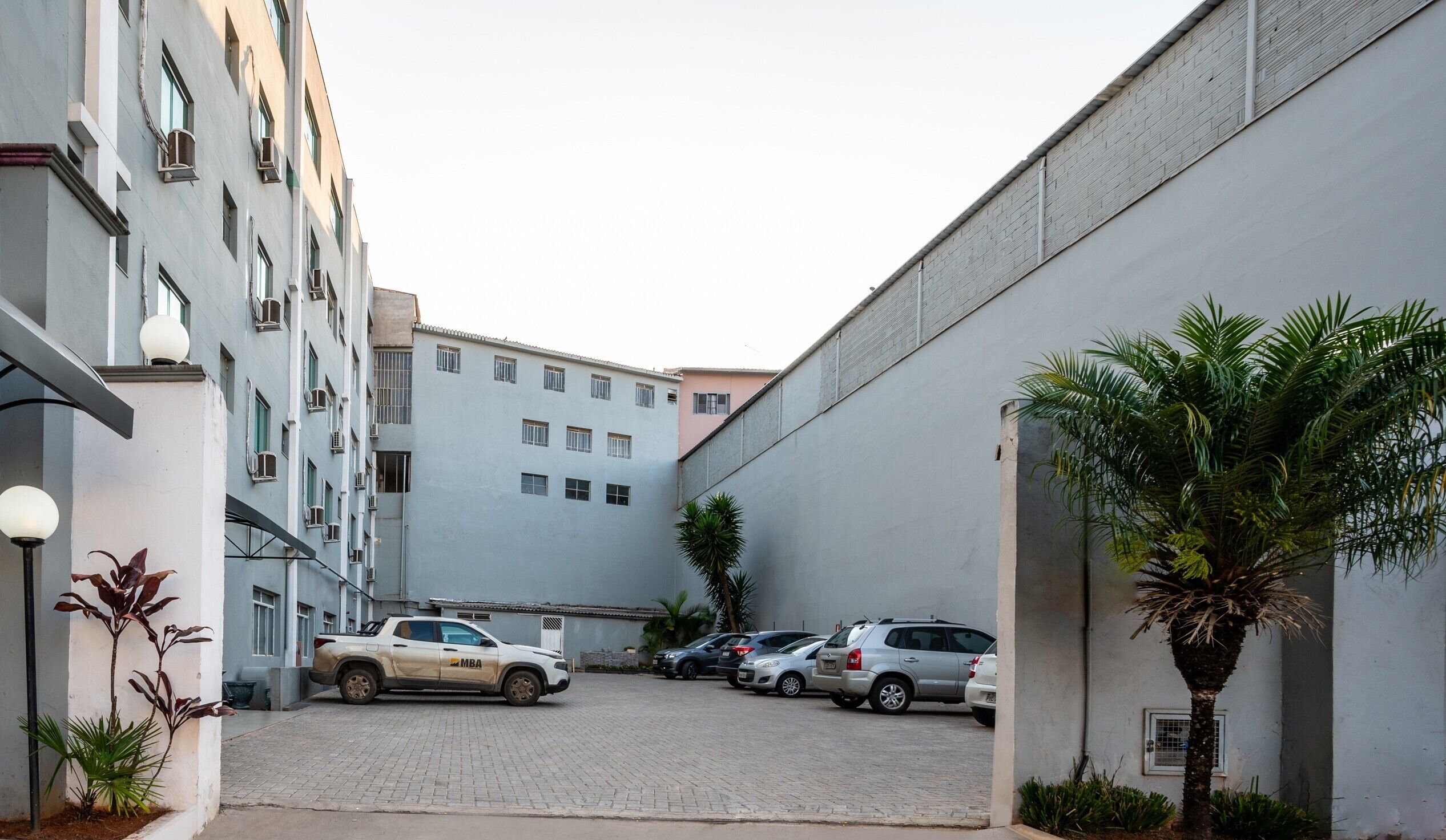 A parking area with several cars, a building with multiple windows, and some potted plants.