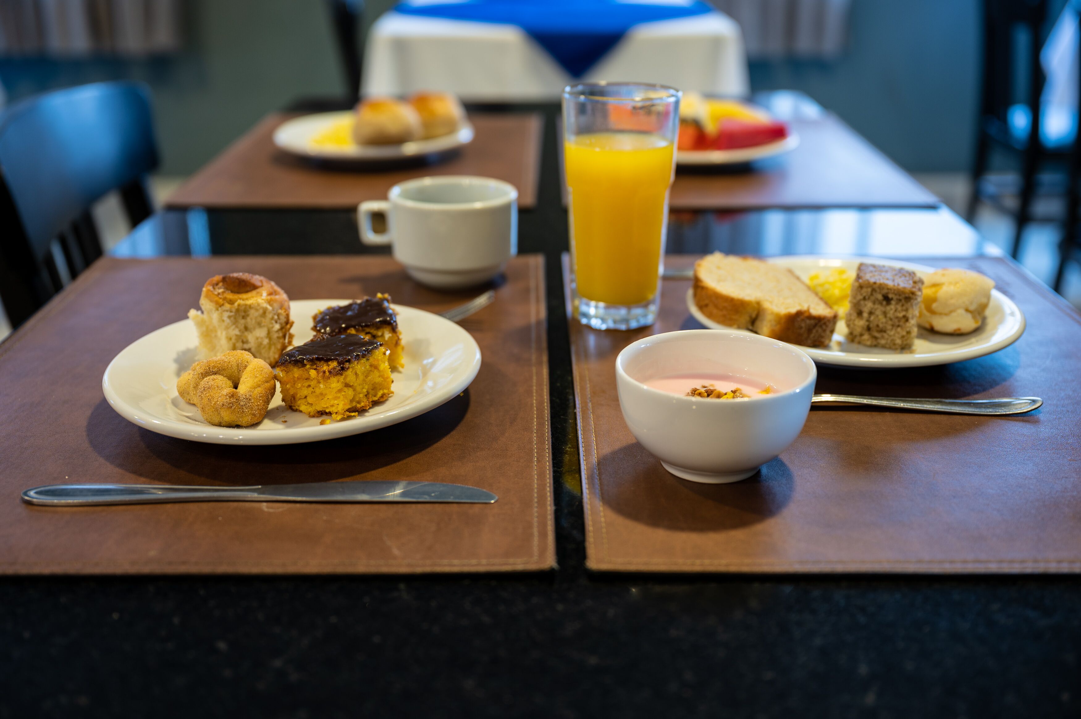 A breakfast setting with plates of food, a glass of orange juice, and a bowl of yogurt.