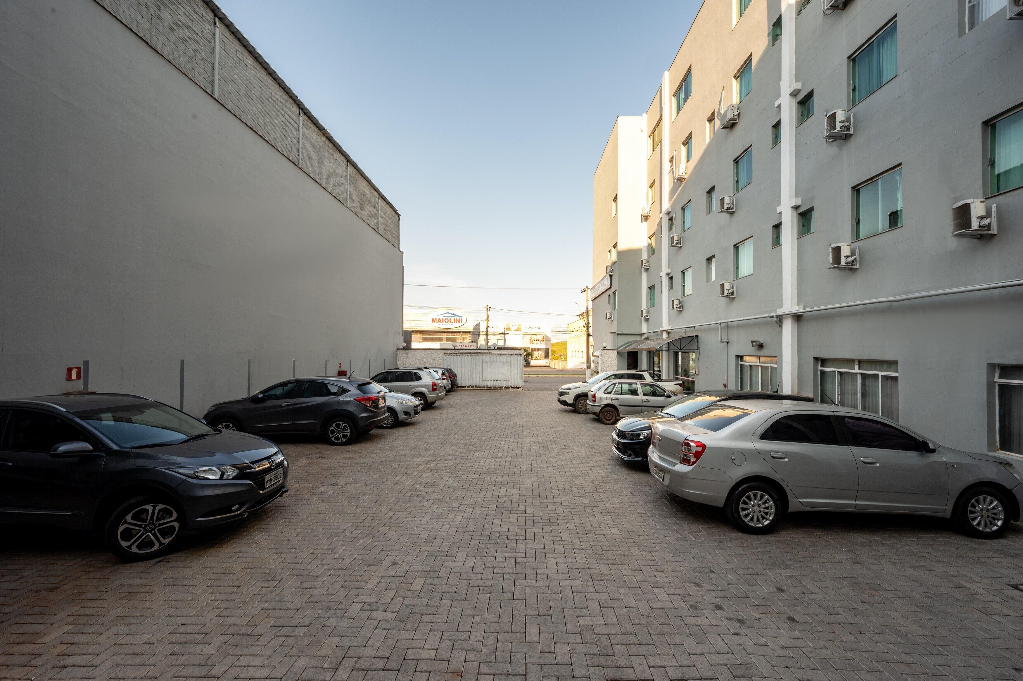 Un estacionamiento con varios coches aparcados frente a un edificio con múltiples ventanas y unidades de aire acondicionado.