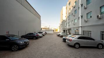 Un estacionamiento con varios coches aparcados frente a un edificio con múltiples ventanas y unidades de aire acondicionado.