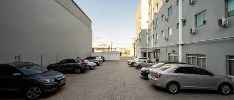 A parking area with several cars parked in front of a building with multiple windows and air conditioning units.