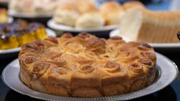Um bolo redondo com um desenho espiralado sobre um prato de prata, rodeado por outras guloseimas assadas.