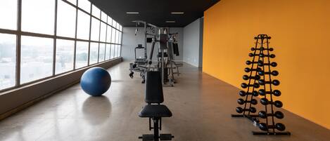 Un gimnasio con equipo de ejercicio, una pelota de ejercicio azul y un soporte para mancuernas.