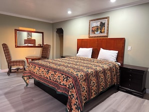 Une chambre bien rangée, avec un grand lit, une chaise, une petite table et une commode.