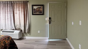 Ein Zimmer mit Tür, Klimaanlage, einem Fenster mit Vorhängen und einem Bilderrahmen an der Wand.