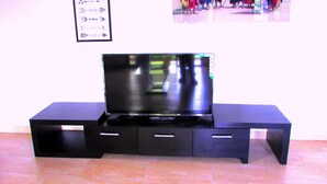 Un mueble bajo negro para televisión con un televisor de pantalla plana, dos cajones y un estante.