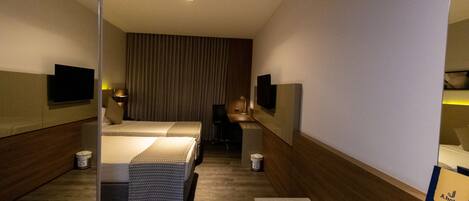 A hotel room with a bed, a desk, a chair, a television, and a minibar.
