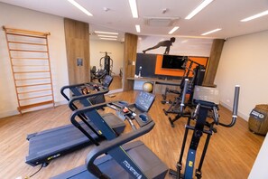Un gimnasio con cintas de correr, elípticas y un televisor montado en la pared.