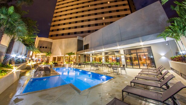 Zona de piscina nocturna con sillones de descanso, piscina y un edificio de diseño moderno.