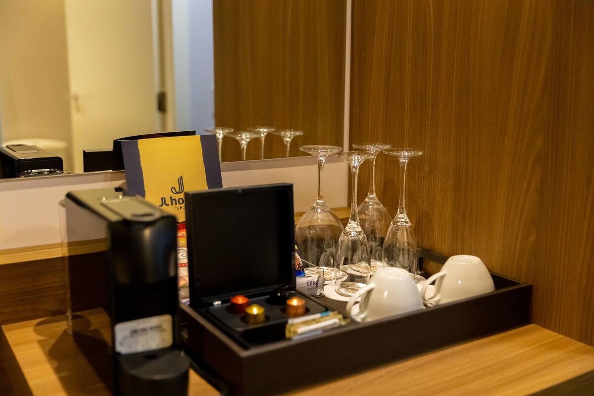 Habitación de hotel con un minibar que contiene una cafetera, una copa de vino y una bandeja con varias copas y vasos.
