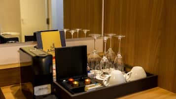 Habitación de hotel con un minibar que contiene una cafetera, una copa de vino y una bandeja con varias copas y vasos.