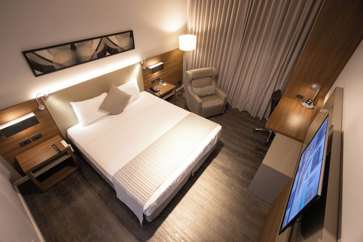 Una habitación de hotel con una cama grande, una silla, un escritorio con computadora y un televisor.