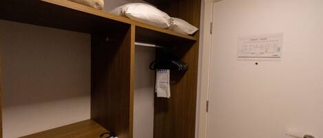 A hotel room with a wooden shelf, a white door, and a notice on the wall.