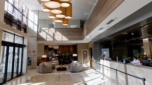 Un hall espacioso con techo alto, luminarias modernas y un mostrador de recepción.