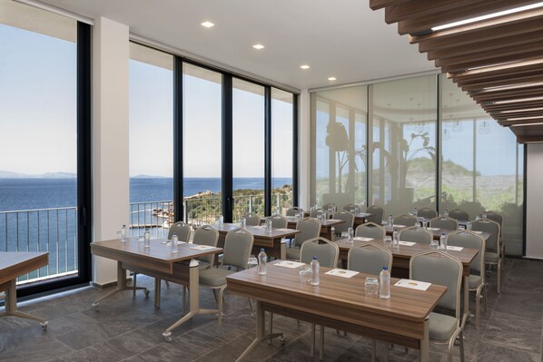 Un salón de conferencias con vista al mar, equipado con mesas, sillas y botellas de agua.