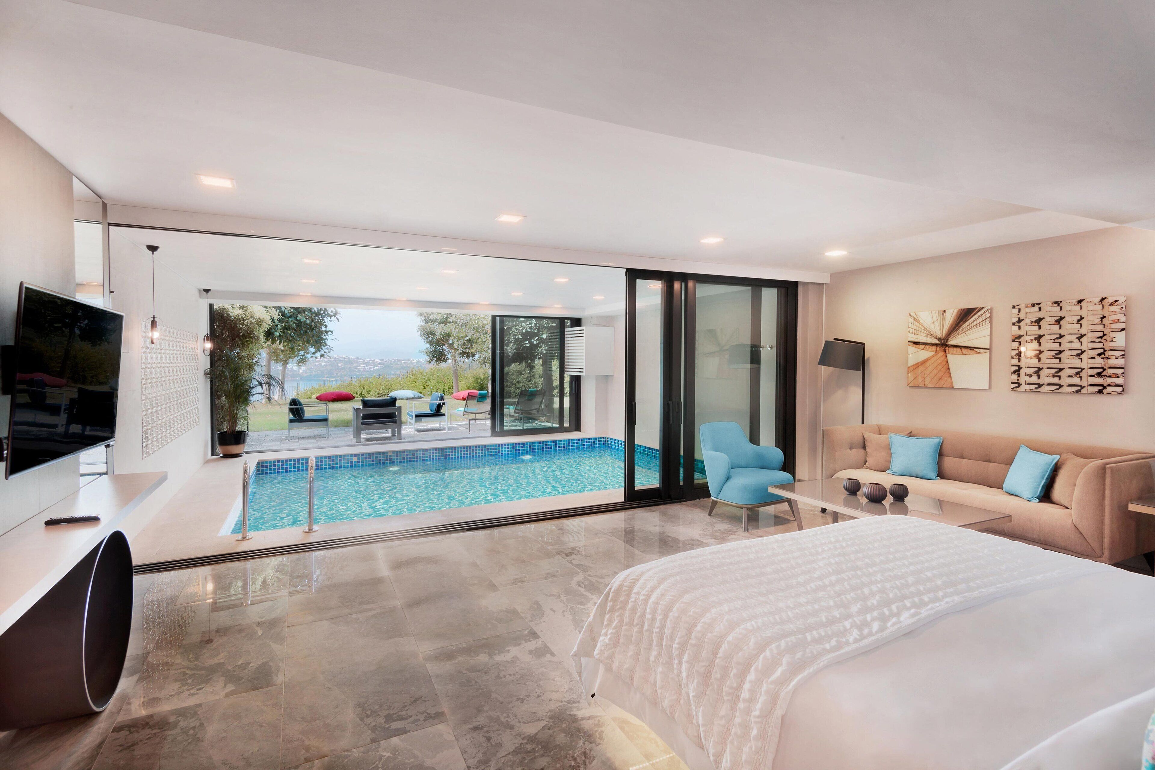 A modern bedroom with a large bed, a TV, and a view of a swimming pool and outdoor seating area.