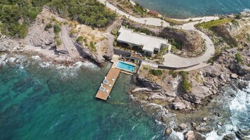 Vista aérea de una propiedad costera con piscina, una casa grande y un litoral rocoso.