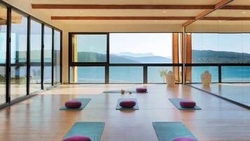 Amplia habitación con ventanas grandes que ofrecen vistas al mar y a las montañas. Hay esterillas de yoga y cojines dispuestos para usarlos.