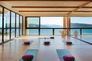 Amplia habitación con ventanas grandes que ofrecen vistas al mar y a las montañas. Hay esterillas de yoga y cojines dispuestos para usarlos.