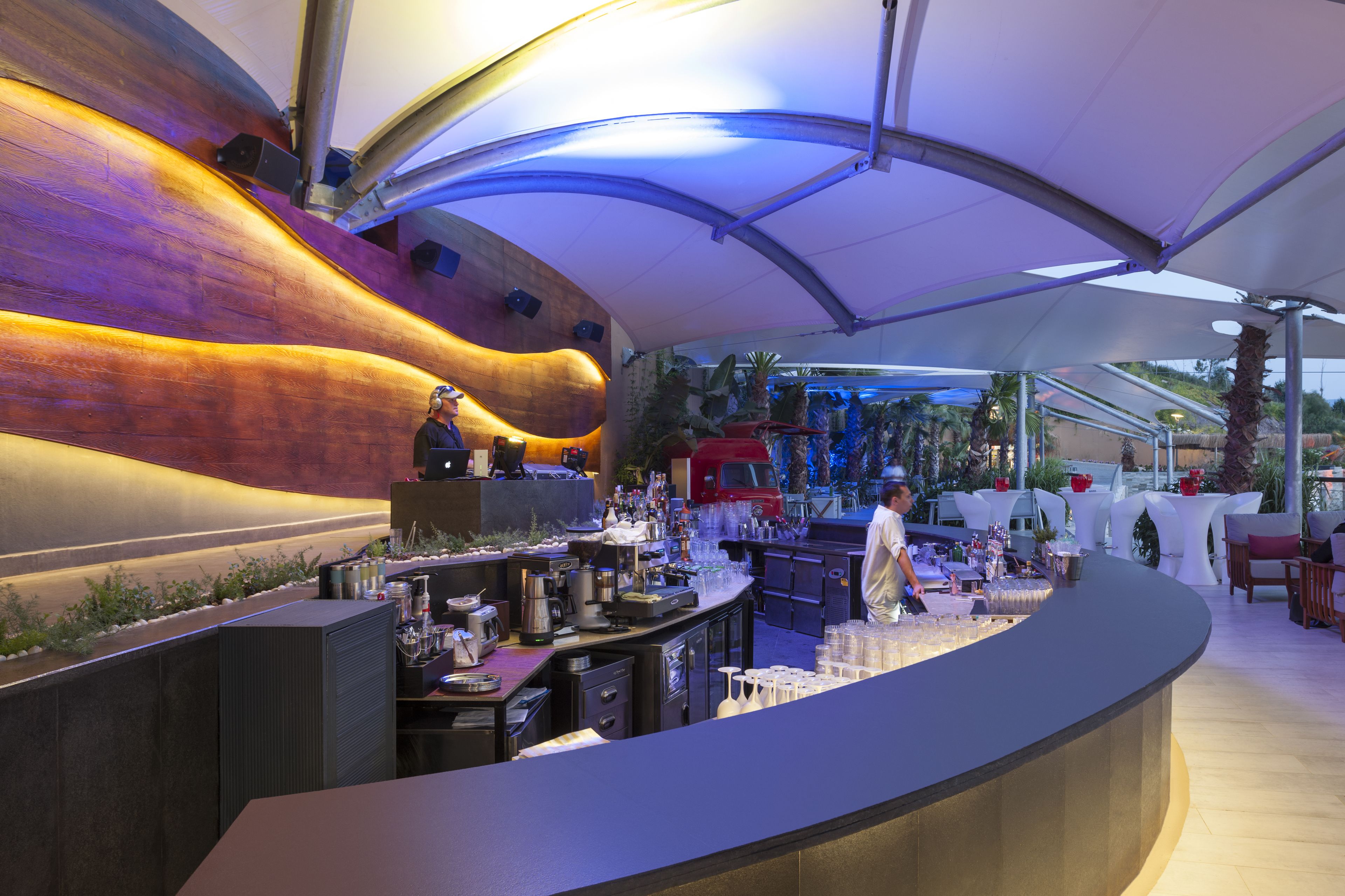 A modern bar area with a curved counter, bar stools, and a seating area with tables and chairs.