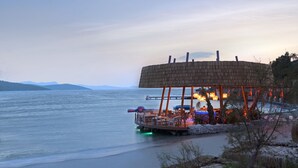 A waterfront restaurant with a circular wooden structure, outdoor seating, and a view of the water. - Le Méridien Bodrum Beach Resort (Milas)