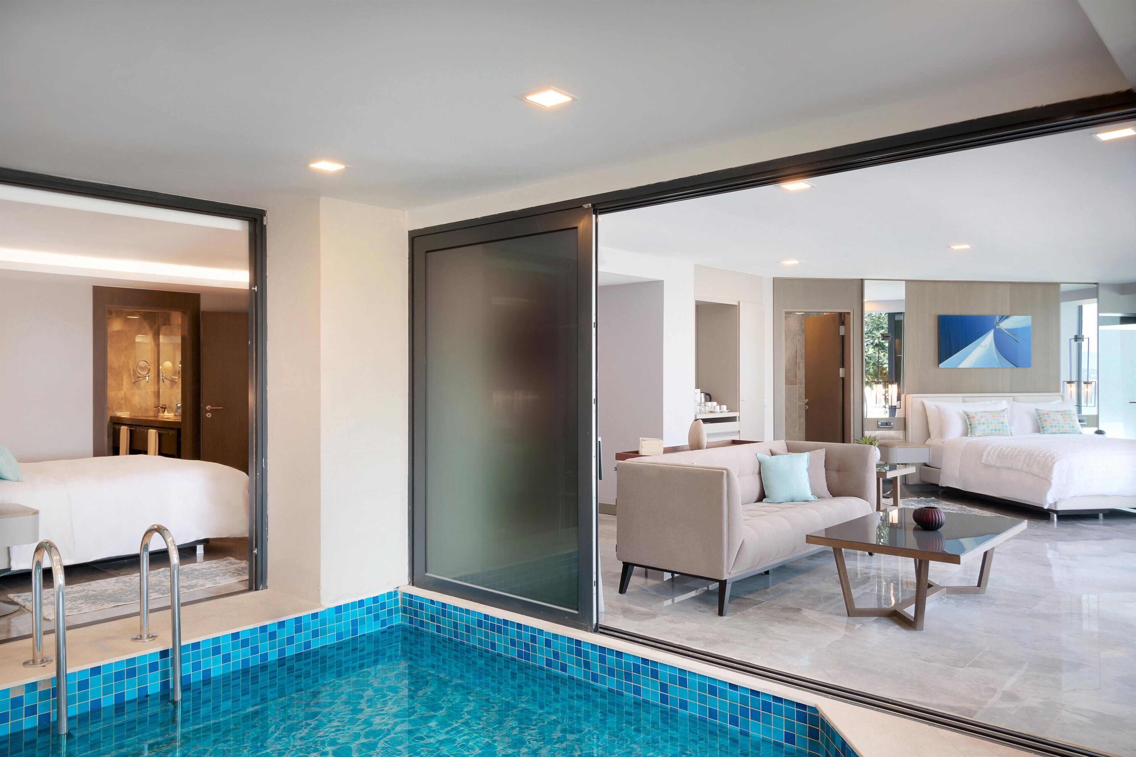 Een moderne hotelkamer met een glazen deur naar een zwembad, een bank, een bijzettafeltje en een bed.