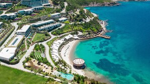 An aerial view of a coastal resort with multiple buildings, a beach, and a swimming pool. - Le Méridien Bodrum Beach Resort (Milas)