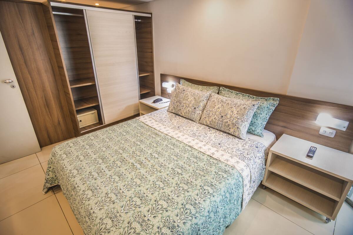 Quarto com cama, mesa de cabeceira, armário e luminária na parede.