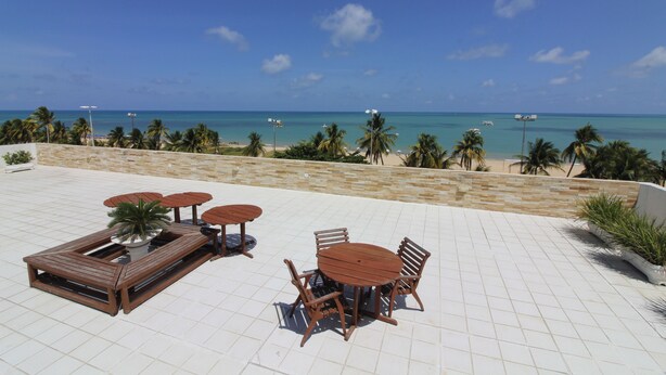 Una terraza en la azotea con una mesa y sillas de madera, un área de descanso con mesa de billar y vistas a la playa y al océano.