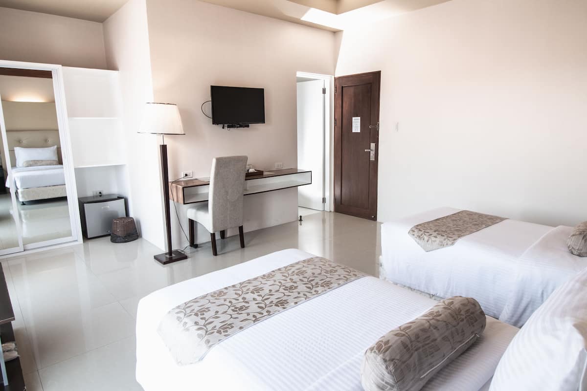 A hotel room with two beds, a desk, a chair, a TV, and a wardrobe.