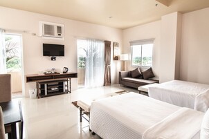 A hotel room with two beds, a TV, a desk with a coffee maker, and a sofa.