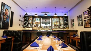 Un restaurante con una larga mesa de madera dispuesta para comer, sillas de cuero negro y una zona de bar con estantes llenos de botellas.